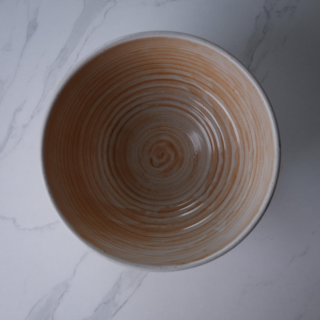 Top-down view of a brown ceramic bowl with concentric ridges on a light marble surface