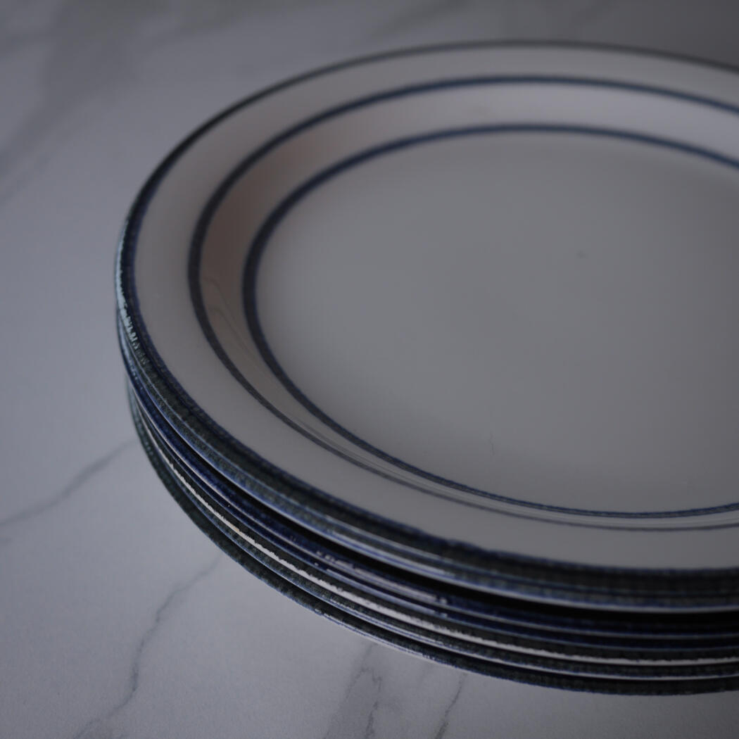 Stack of white plates with dark blue rims on a marble surface, close-up view.