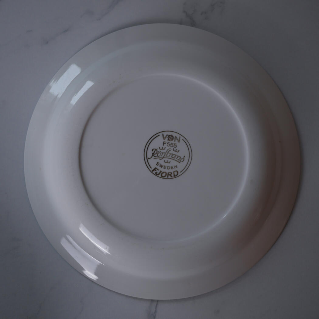 Bottom of a white ceramic plate with a circular maker's mark stamped in the center on a marble surface.