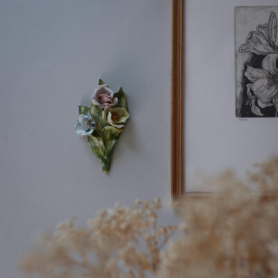 Pastel flower cluster on a green leaf backing mounted on a gray wall, beside a wooden-framed black-and-white botanical print.