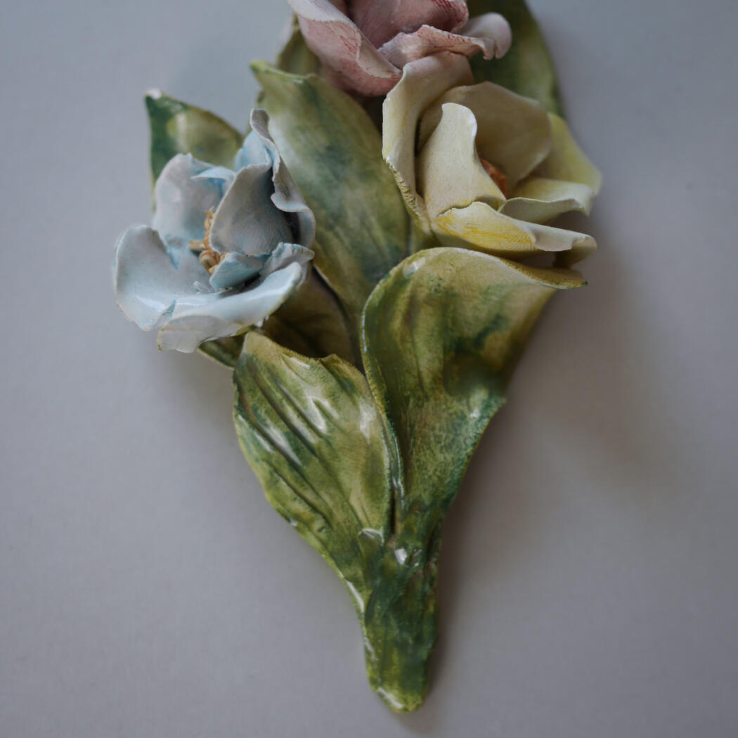 Dried, multicolored flower with blue, yellow, and pink petals and green leaves on a gray background