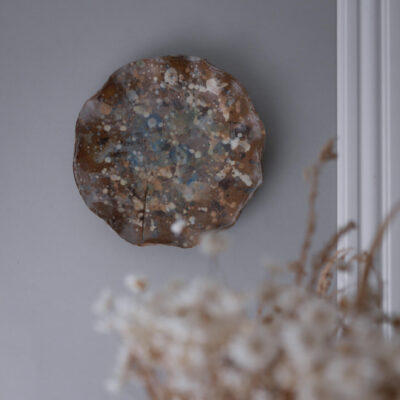 Round decorative ceramic plate with blue, white, and brown splatter glaze mounted on a gray wall.