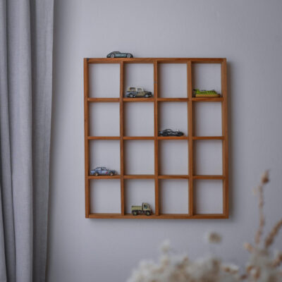 Wooden 4x4 grid shelf mounted on a pale wall with several toy cars placed in the compartments.