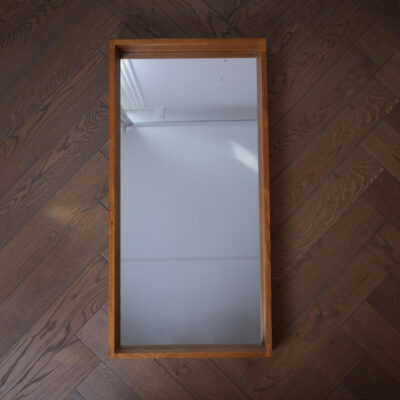 Wooden-framed full-length mirror lying on a dark wood floor, photographed from above, reflecting a white ceiling.