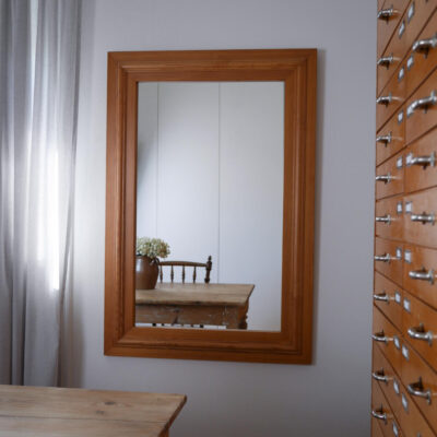 Wooden-framed wall mirror reflecting a rustic wooden table with a vase of white flowers and a chair.