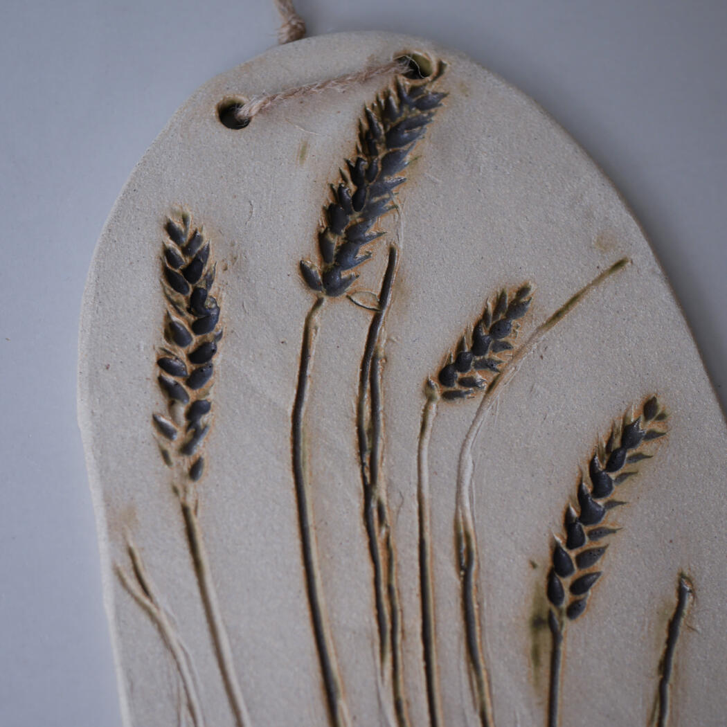 Oval ceramic wall plaque featuring pressed wheat stalks in relief contrasty against the light beige background