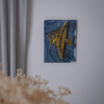 Colorful painting of a fish on a blue background hanging on a light gray wall near curtains.
