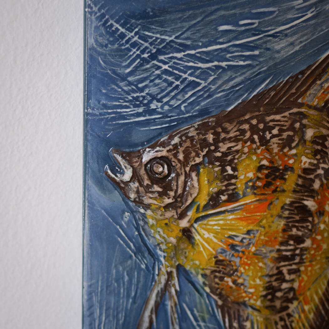 Close-up of a textured painting depicting a colorful fish with yellow and orange scales on a blue background.