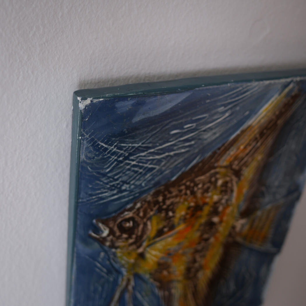 Close-up of a blue-framed painting with a damaged top-left corner and visible surface scratches on the blue background.