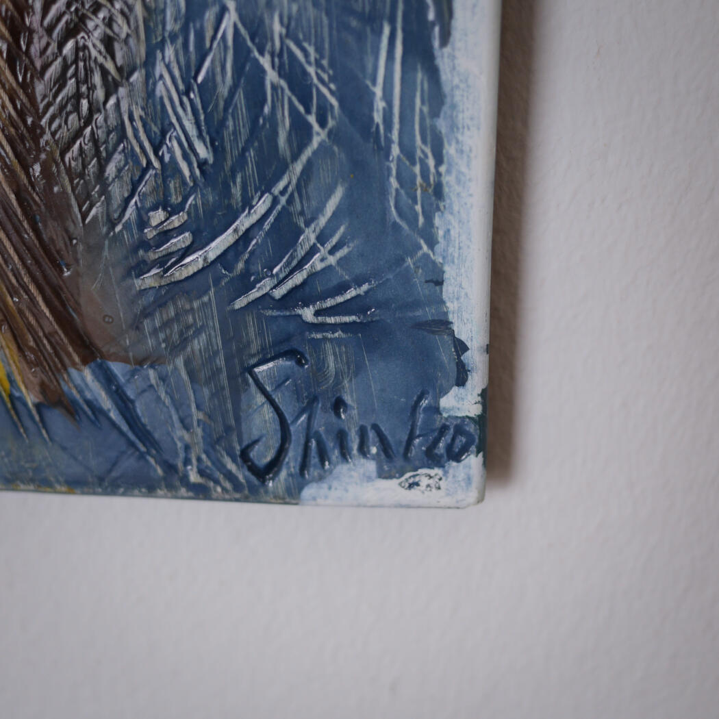 Close-up of a blue abstract painting corner with bold white scratches and a handwritten signature at the bottom edge.