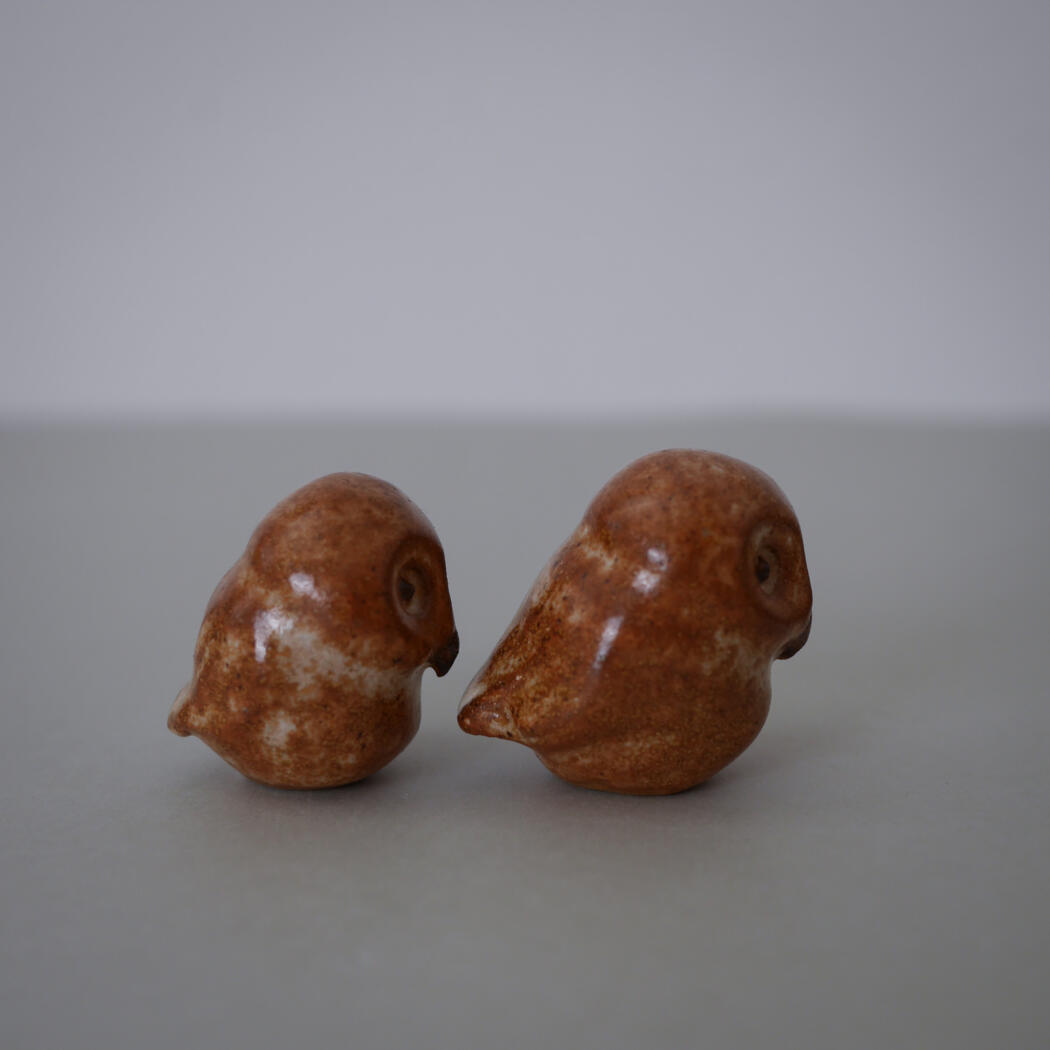 Two small brown ceramic bird figurines facing each other on a light gray tabletop surface.