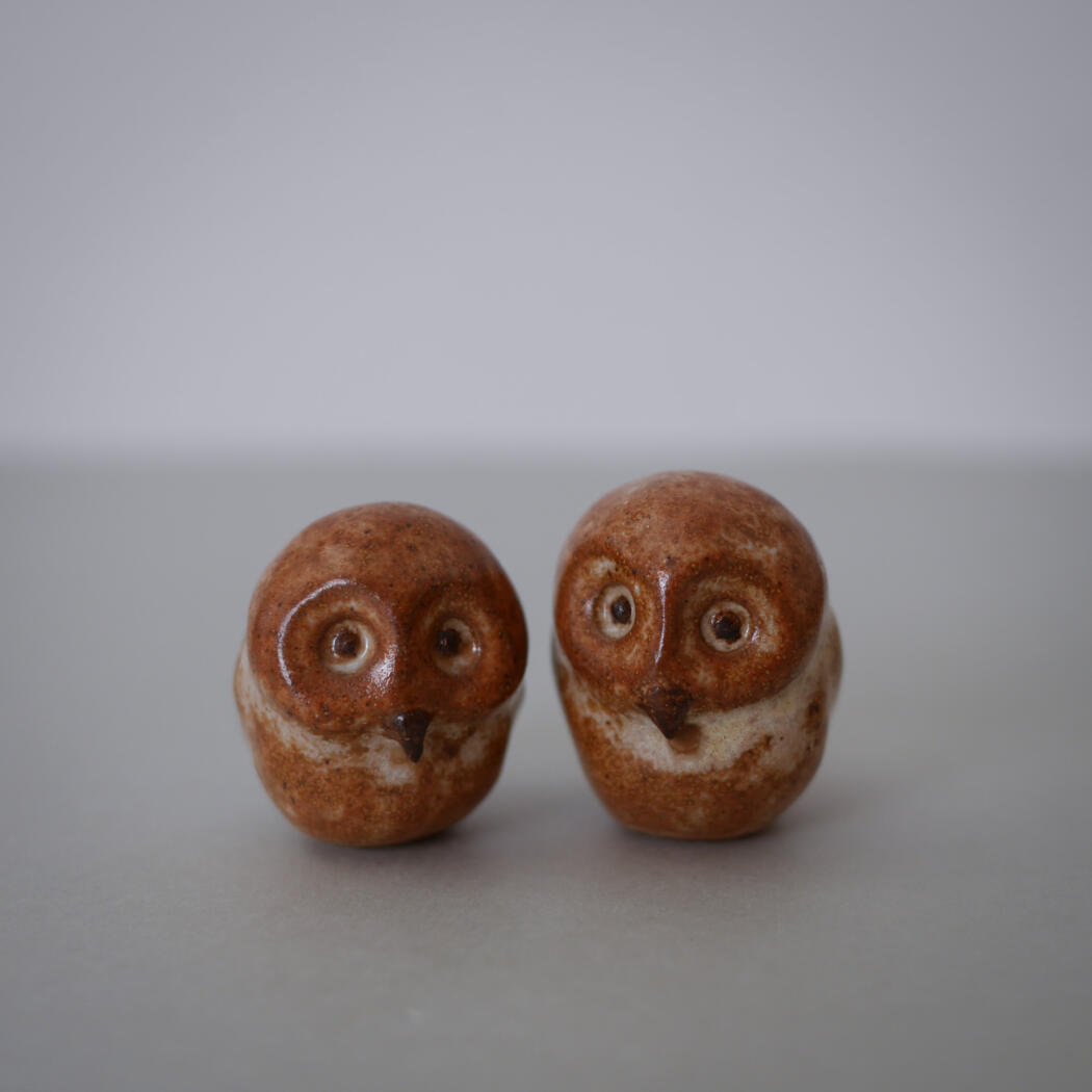 Two small brown ceramic owl figurines with wide eyes on a gray surface.