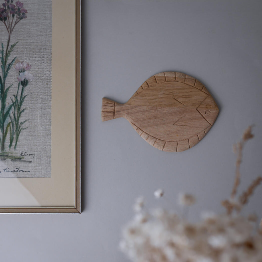 Wooden fish-shaped wall ornament mounted beside a framed botanical print on a gray wall.