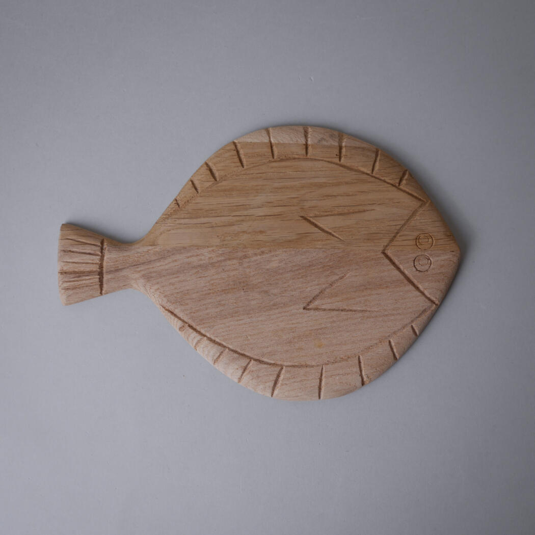 Wooden fish-shaped cutting board with a carved scale pattern on a gray surface.