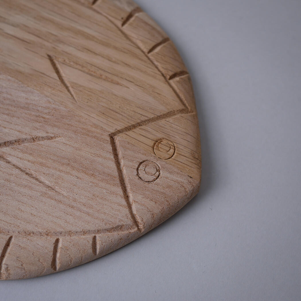Close-up of a round wooden cutting board with carved lines and two circular depressions near the edge.