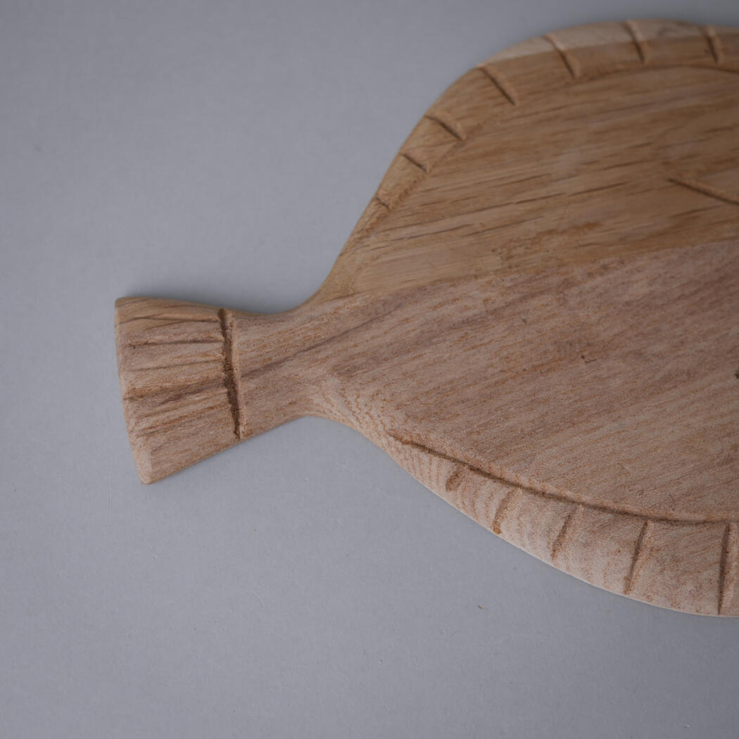 Partial view of a light wooden cutting board with a rounded handle on a gray background.