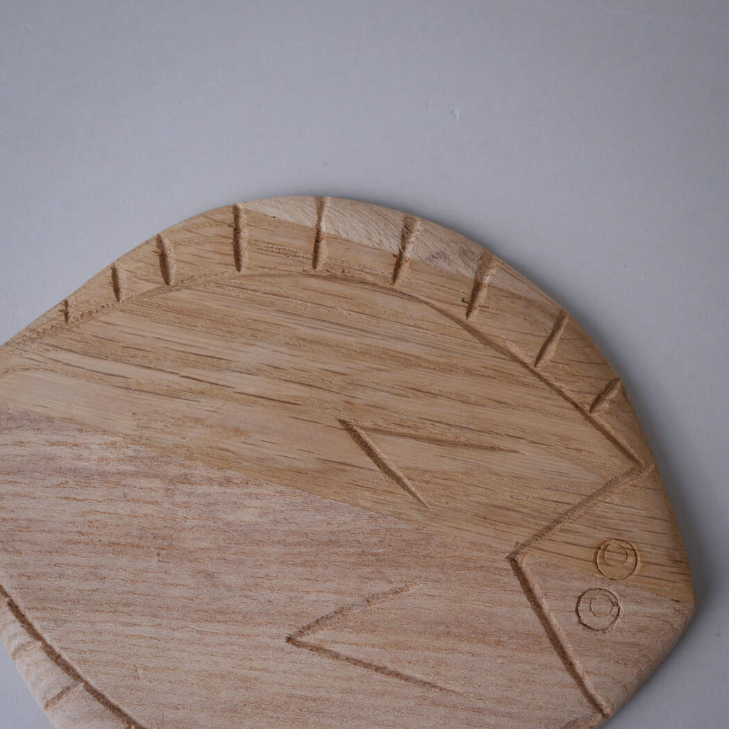 Round wooden cutting board with carved edge notches and subtle grain patterns, placed on a gray surface.