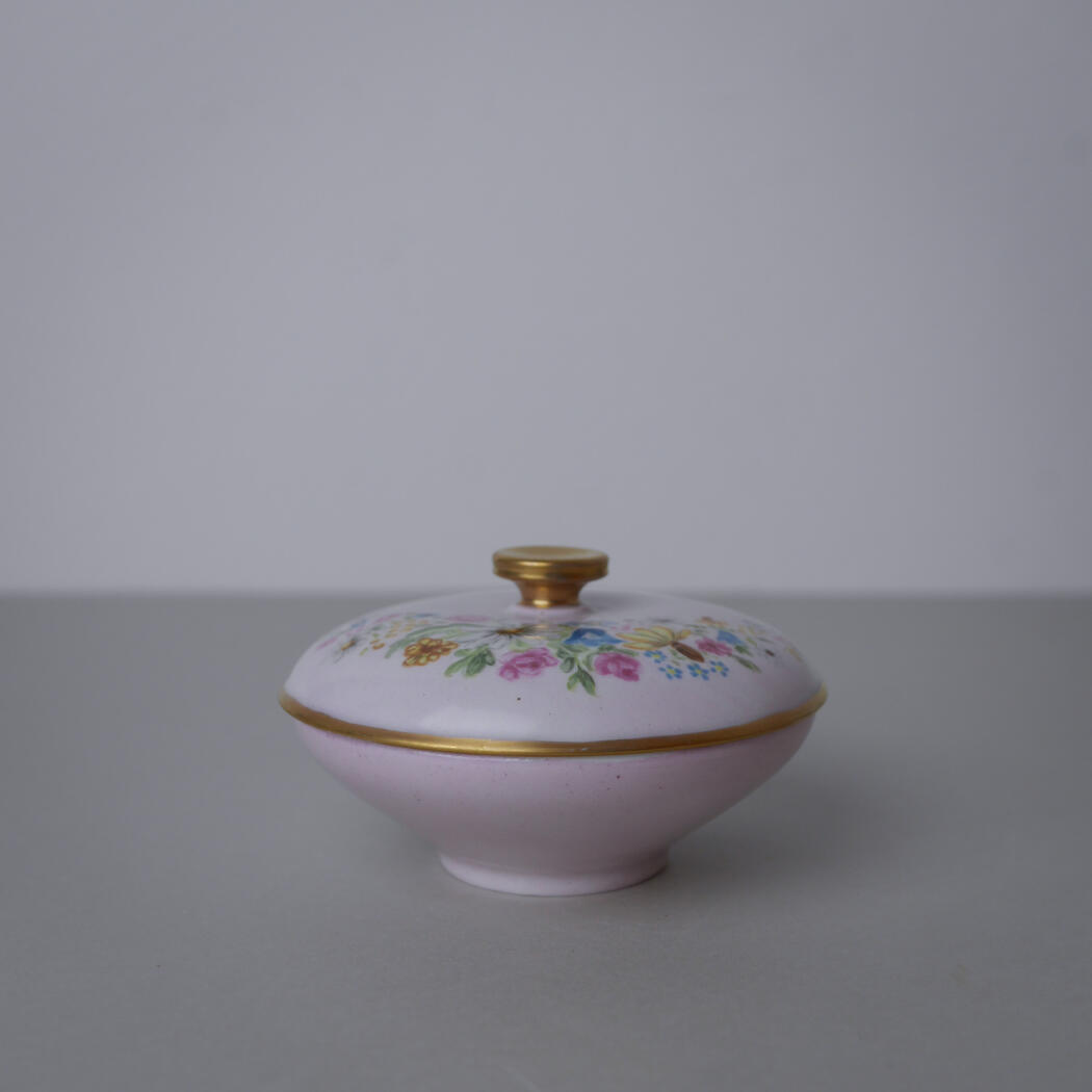 Pink porcelain sugar bowl with a floral pattern and gold trim, lid topped with a small gold knob, on a gray surface.