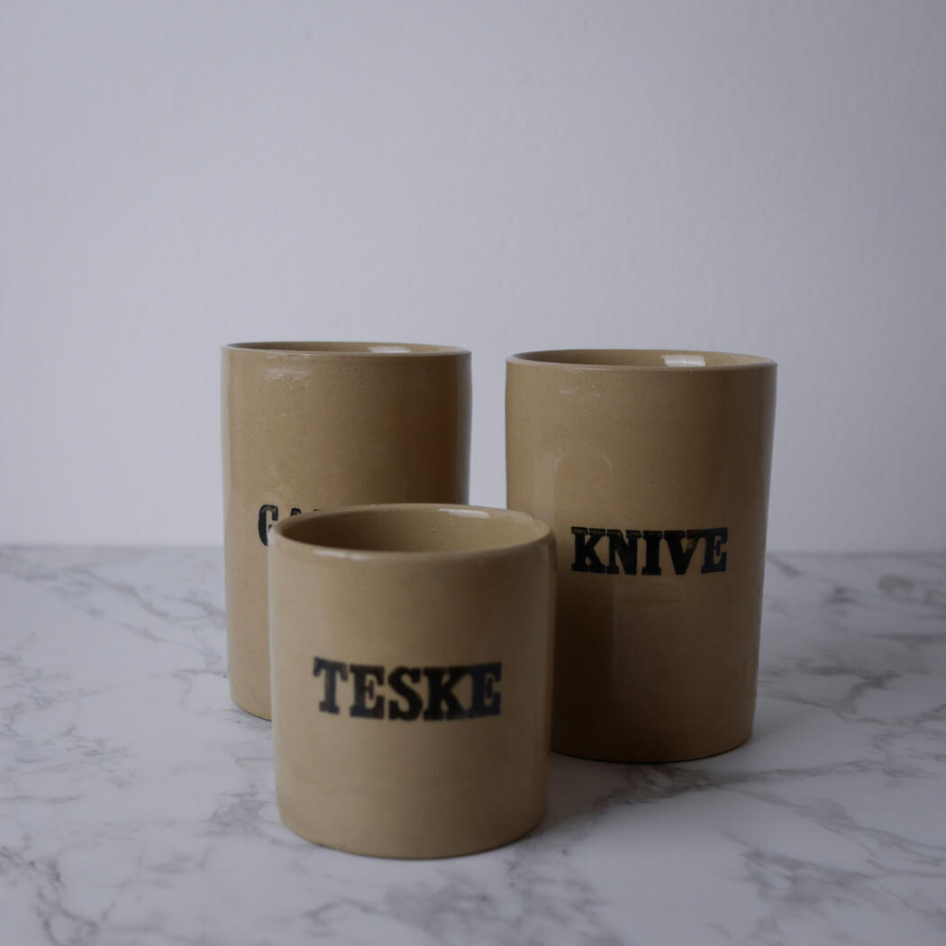 Three beige cardboard cups arranged on a marble counter, with bold black text reading TESKE and KNIVE on their sides.