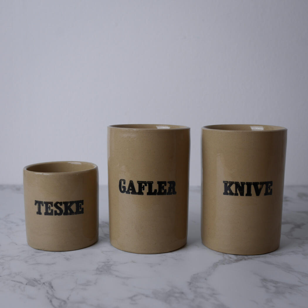Three beige ceramic mugs in a row on a marble surface, each labeled in bold black text: TESKE, GAFLER, KNIVE.