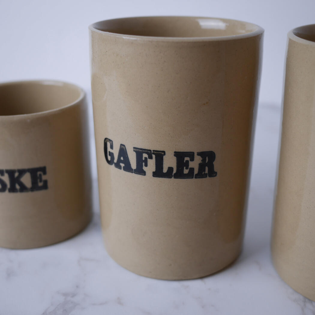 Three beige ceramic mugs on a white surface; the central mug reads 'GAFLER' in bold black letters.