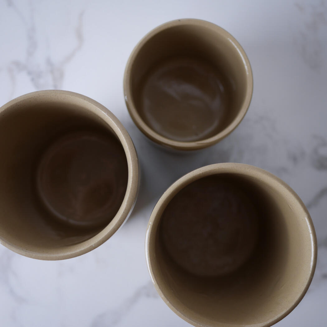 Three beige ceramic cups seen from above on a white marble surface, mostly empty.