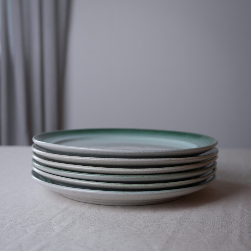 Stack of five ceramic plates with a pale green glaze on a light table.