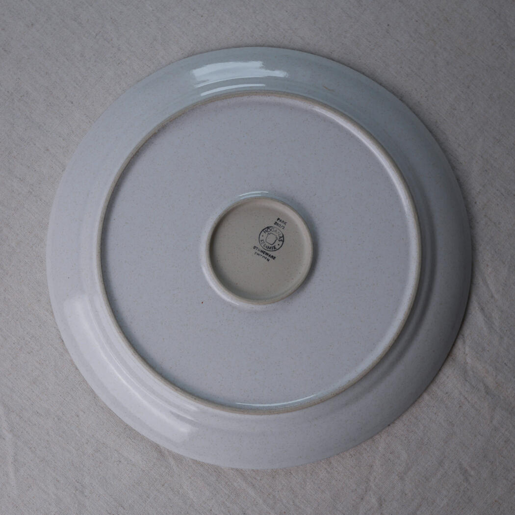 Ceramic plate photographed from the bottom, showing a small maker's mark in the center on a pale base glaze with a blue-gray outer rim.