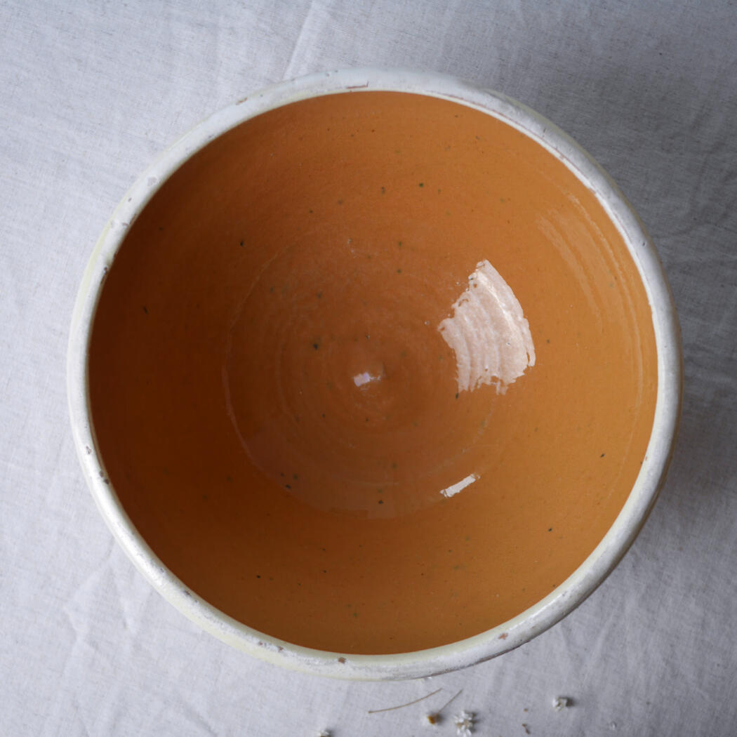 Top-down view of a ceramic bowl filled with orange soup with green specks on a white surface.
