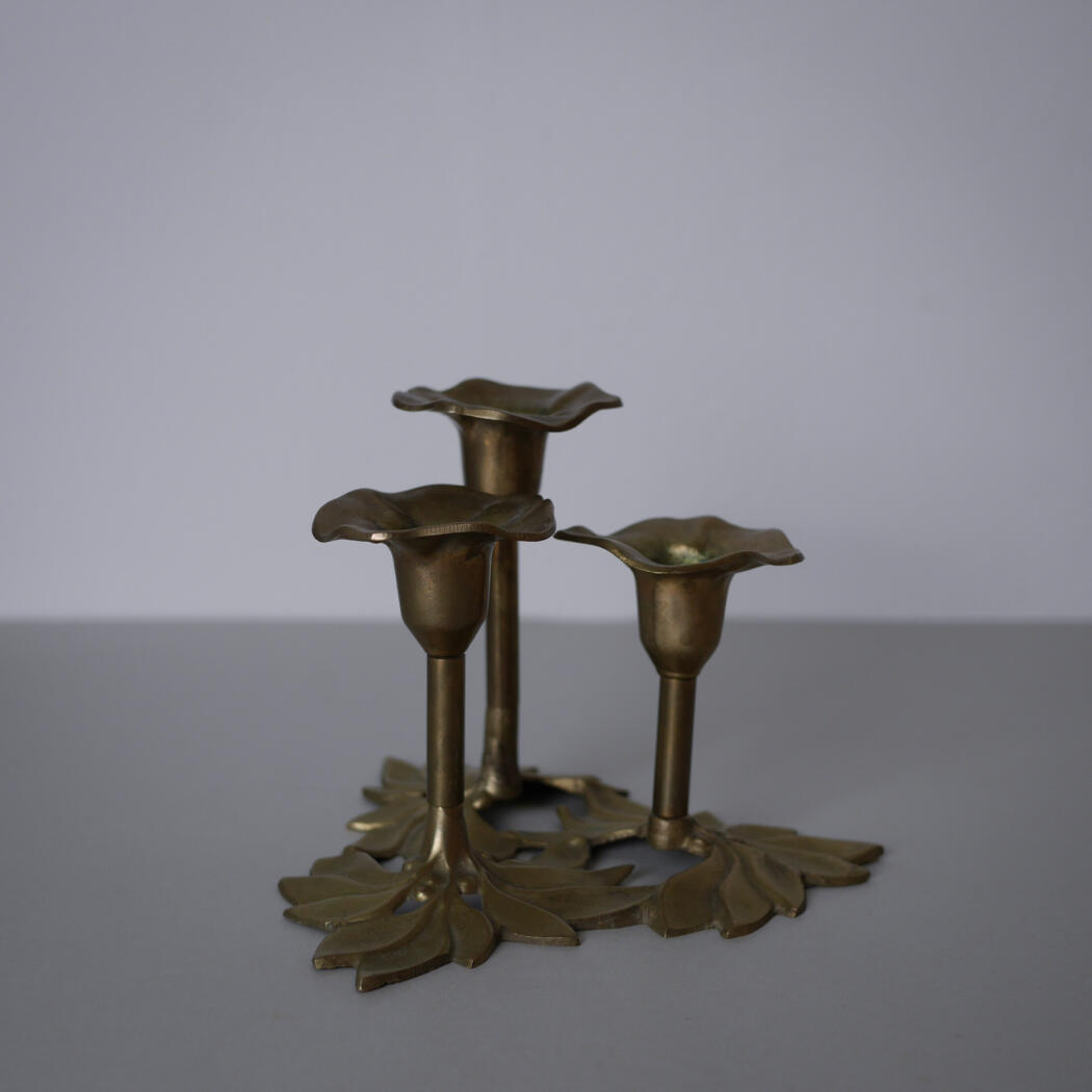 Bronze triple-candle holder with cup-shaped tips and leaf-shaped bases on a flat surface.