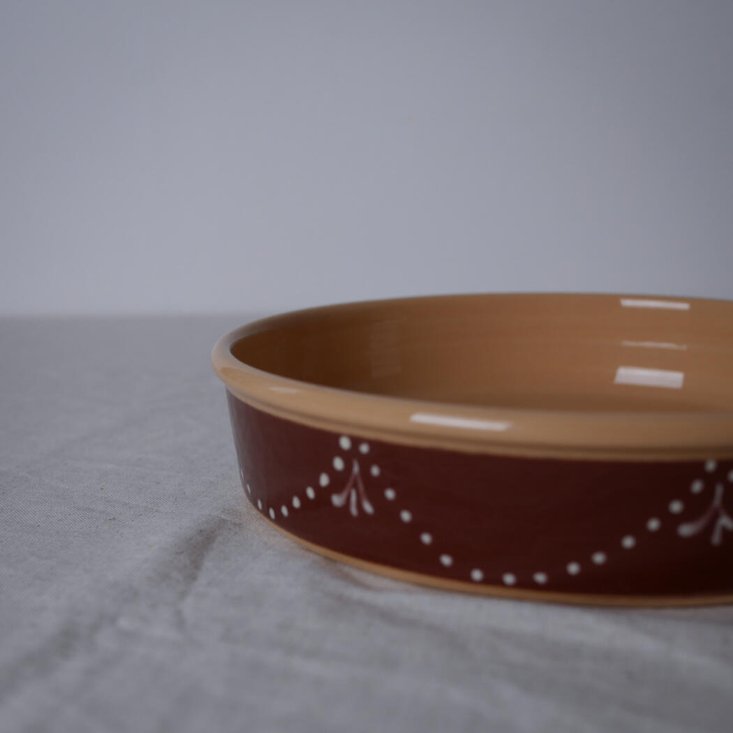 Brown ceramic shallow bowl with a white dotted pattern along the side, placed on a light fabric surface.
