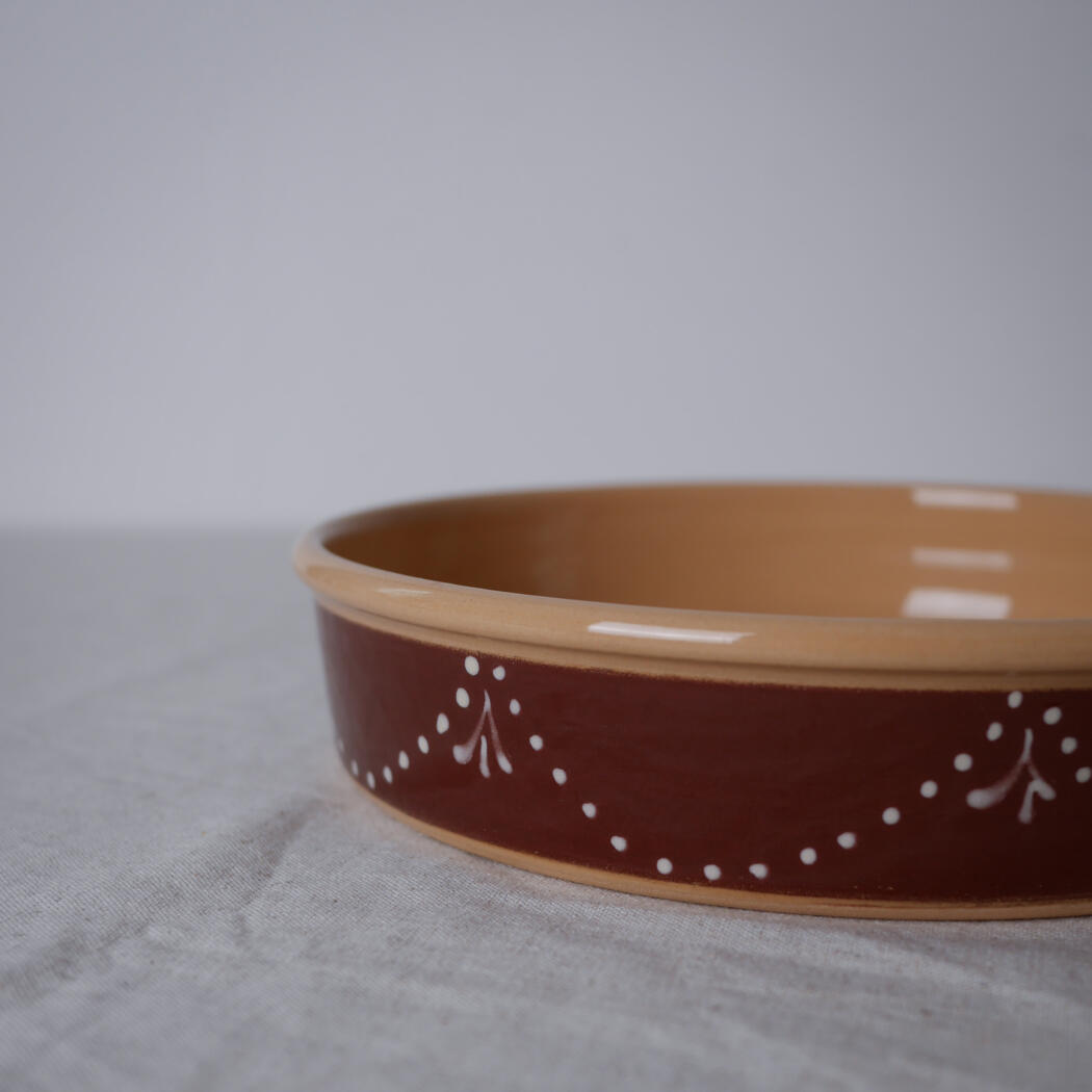 Brown ceramic shallow bowl with a cream rim and white dotted pattern on a light fabric surface, empty and ready to use.