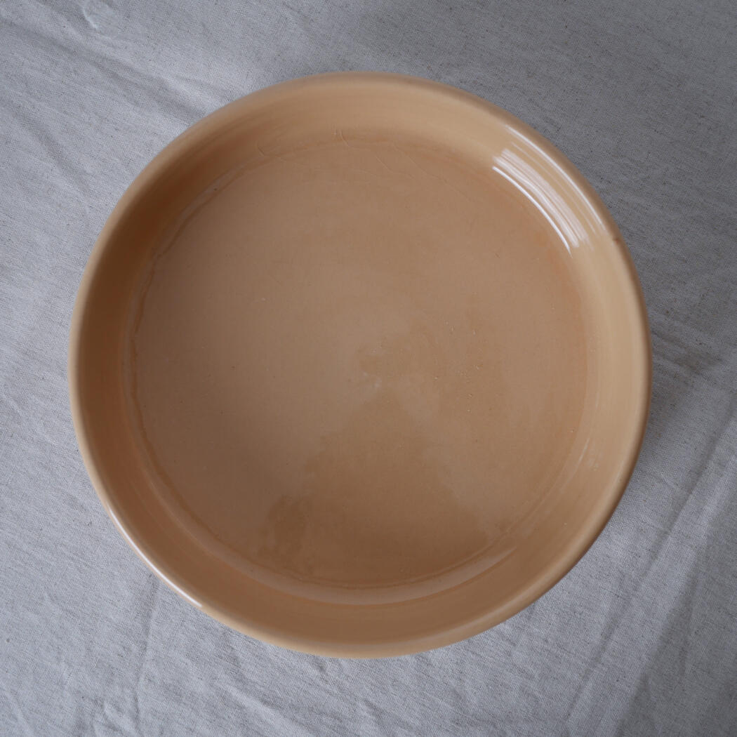 Beige ceramic bowl resting on a light fabric surface, viewed from above.