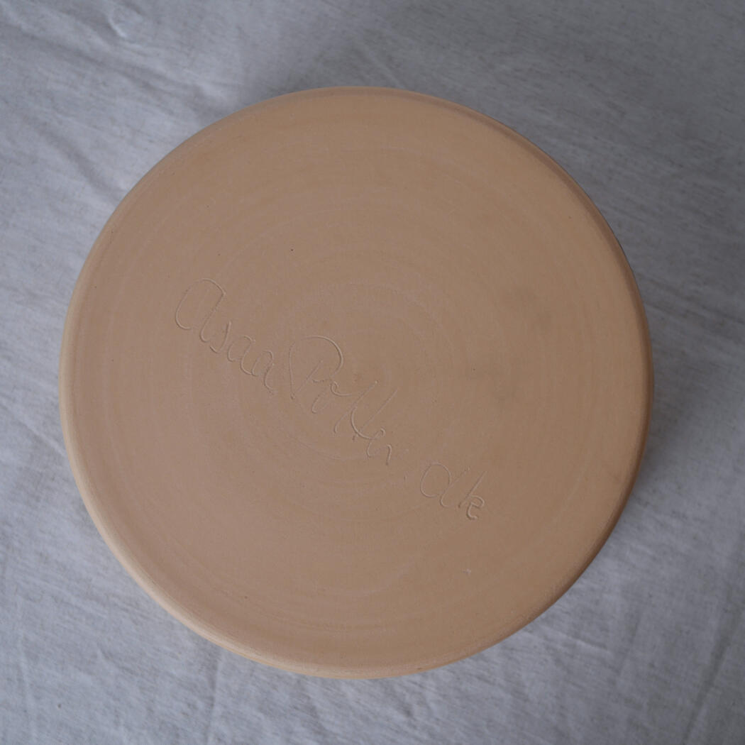 Ceramic plate viewed from bottom with a faint, cursive engraving (signature) on the base.