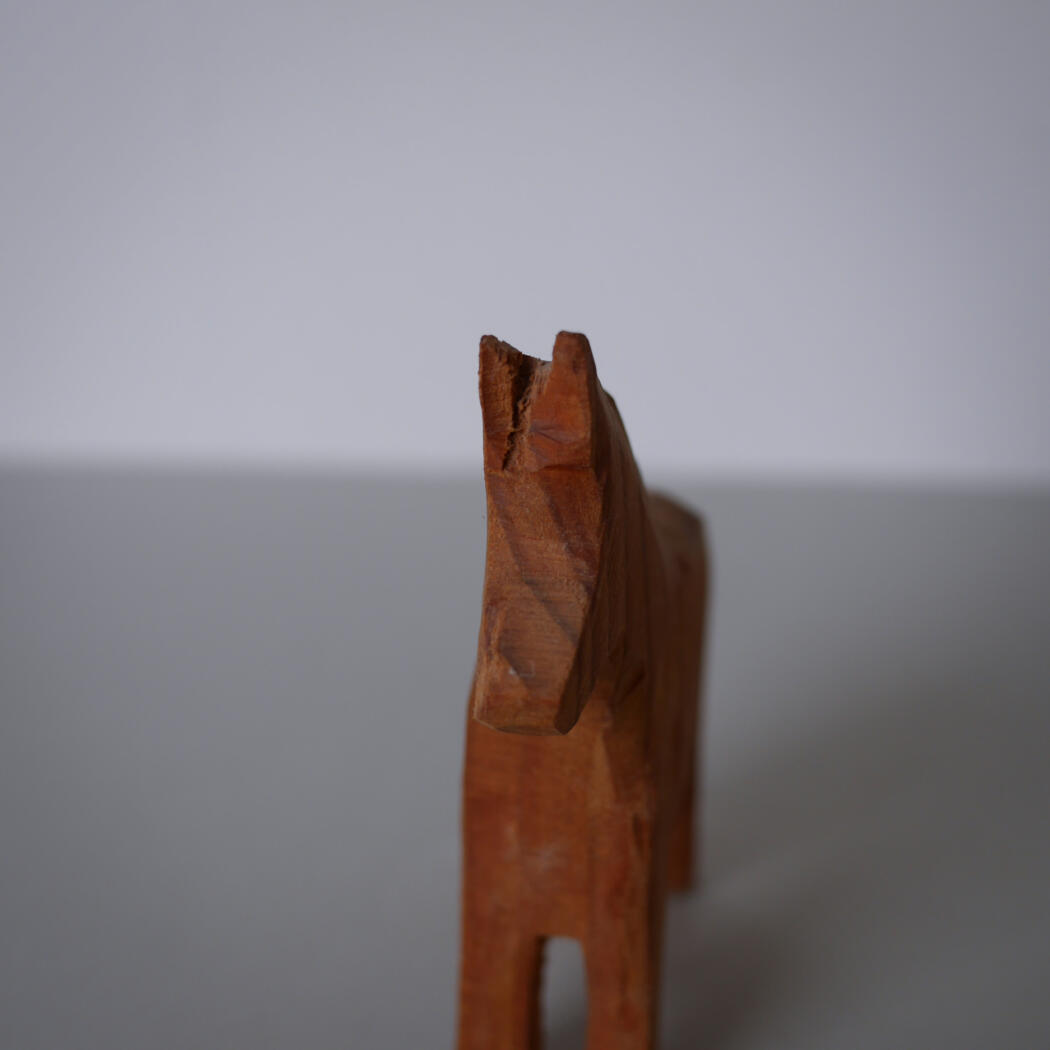 Wooden carved horse figurine in orange-brown, shown from the side against a gray background (decorative object).