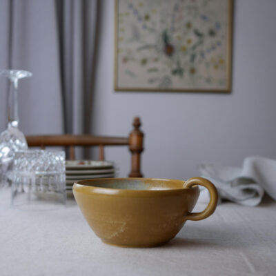 Brown ceramic cup on a white tablecloth in focus, with glassware and plates blurred in the background.