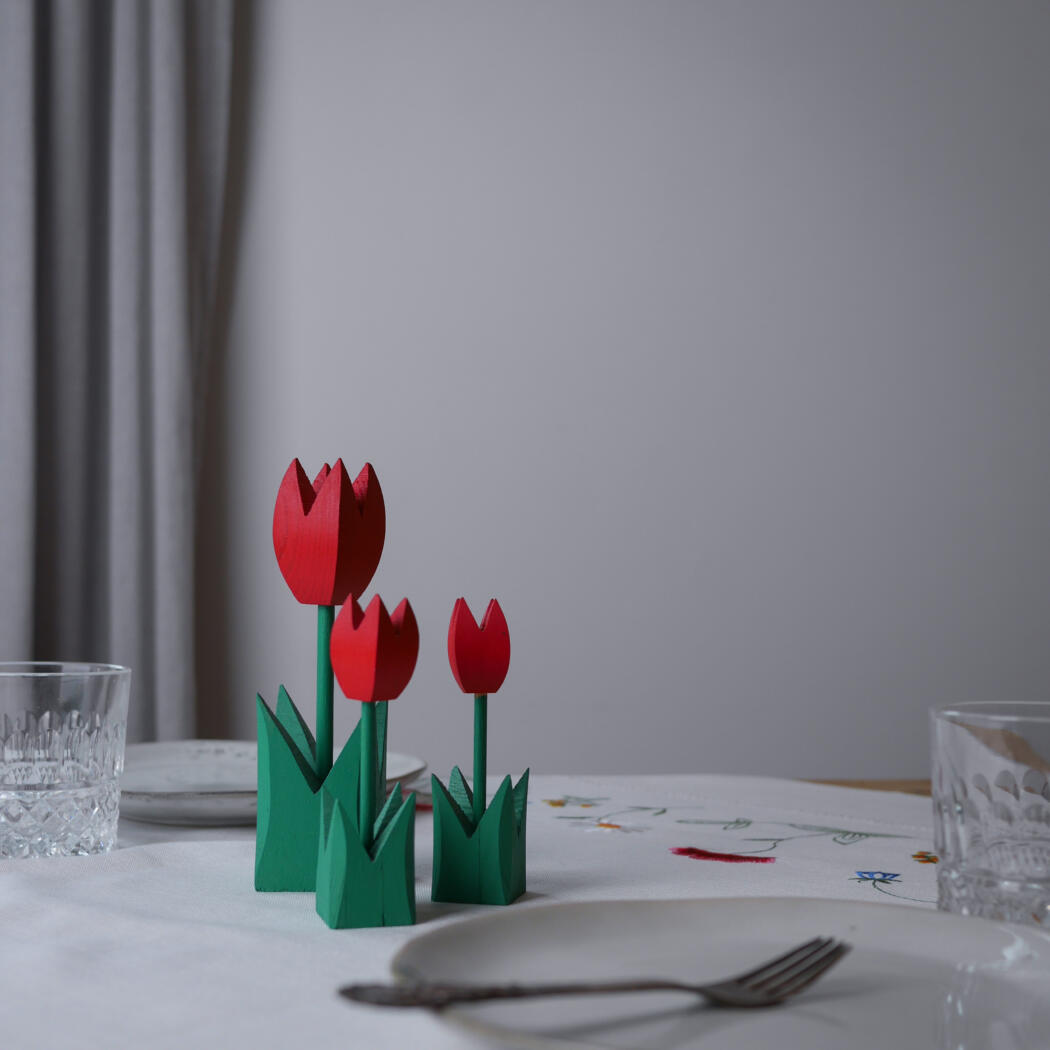 Paper tulip centerpiece with red blooms and green stems on a dining table near glassware and a plate.