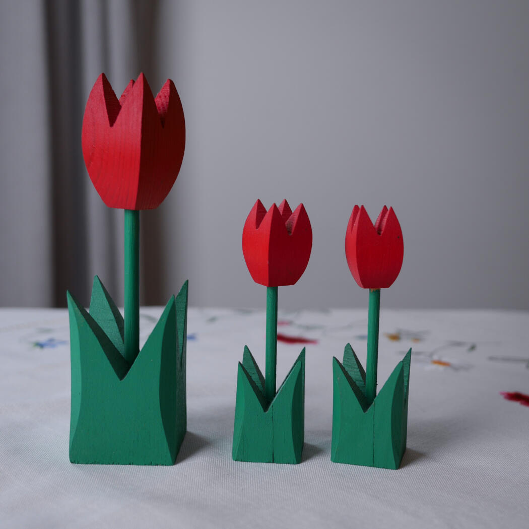 Three wooden tulip decorations with red petals and green stems on a light table surface.