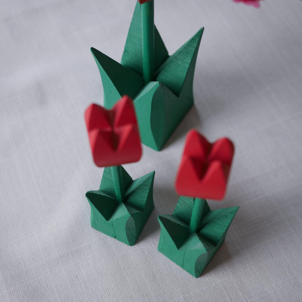 Three origami tulips with green stems and leaves and red petals on a white fabric surface, viewed from above/side angle.