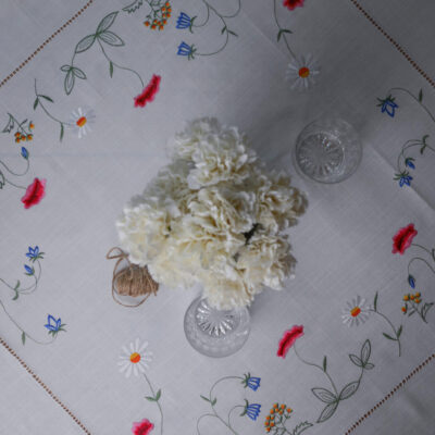 White carnation bouquet centerpiece on an embroidered tablecloth with glassware nearby.