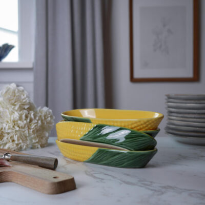 Stack of yellow and green ceramic bowls on a marble kitchen counter with a cutting board and white hydrangea nearby.