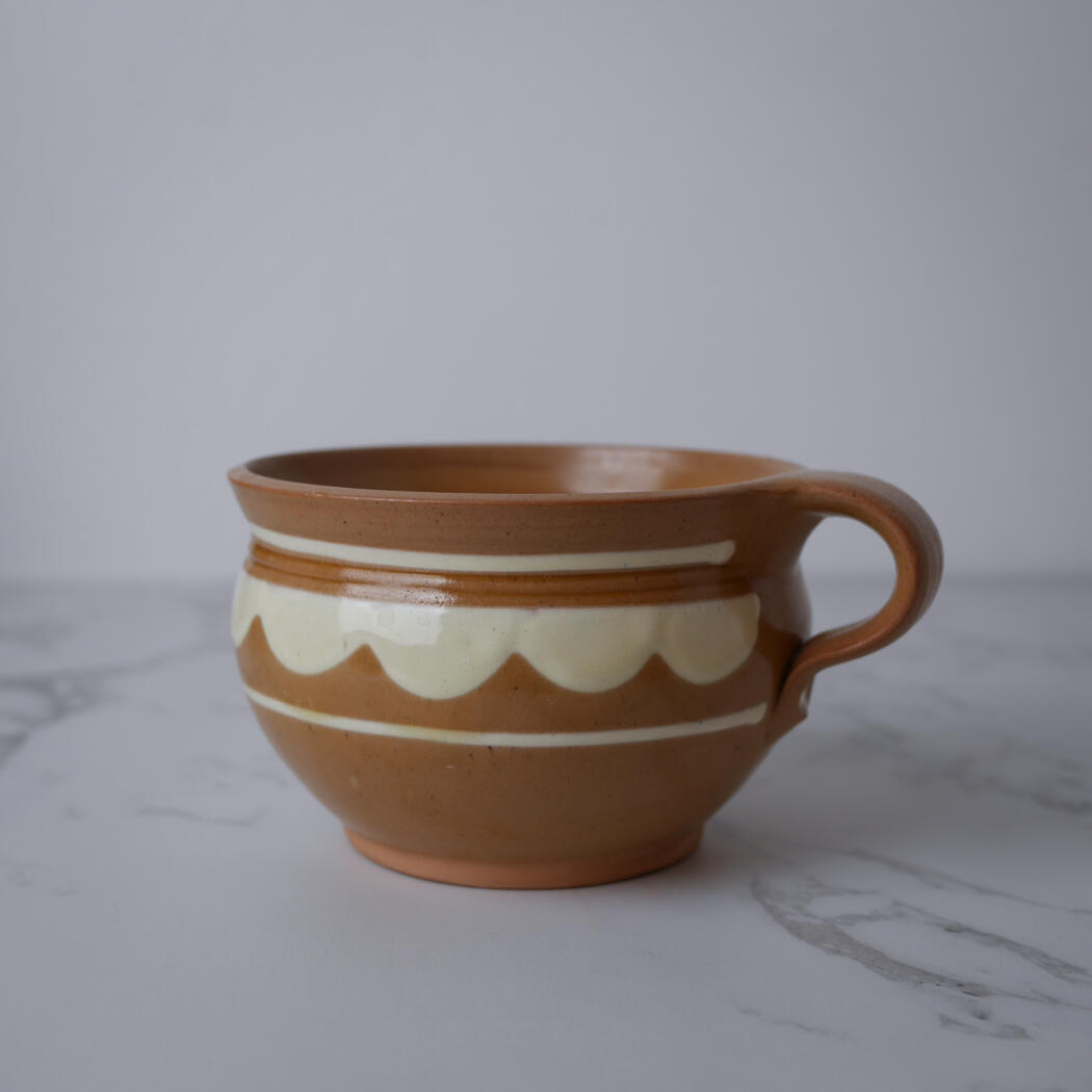 Brown ceramic mug with white decorative bands on a marble surface.