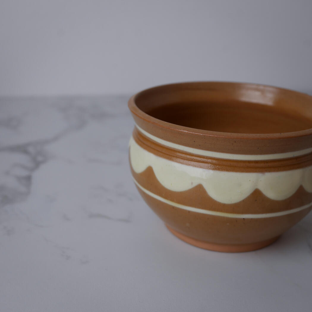 Terracotta ceramic pot with cream wavy stripes on a marble surface, shown in partial side view.