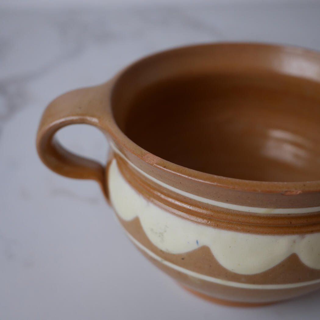Close-up of a terracotta ceramic pot with a curved handle and cream decorative banding, showing earthy tones.