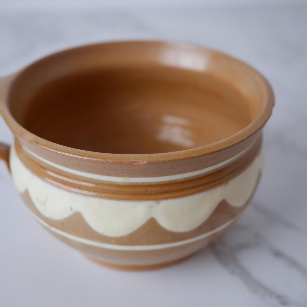 Brown and cream ceramic pot with a white scalloped band, empty and sitting on a light marble surface