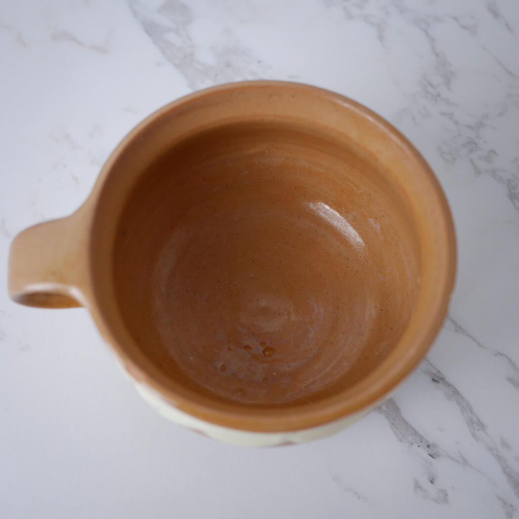 Top-down view of a brown ceramic mug with a handle on the left, sitting on a white marble surface, empty inside.