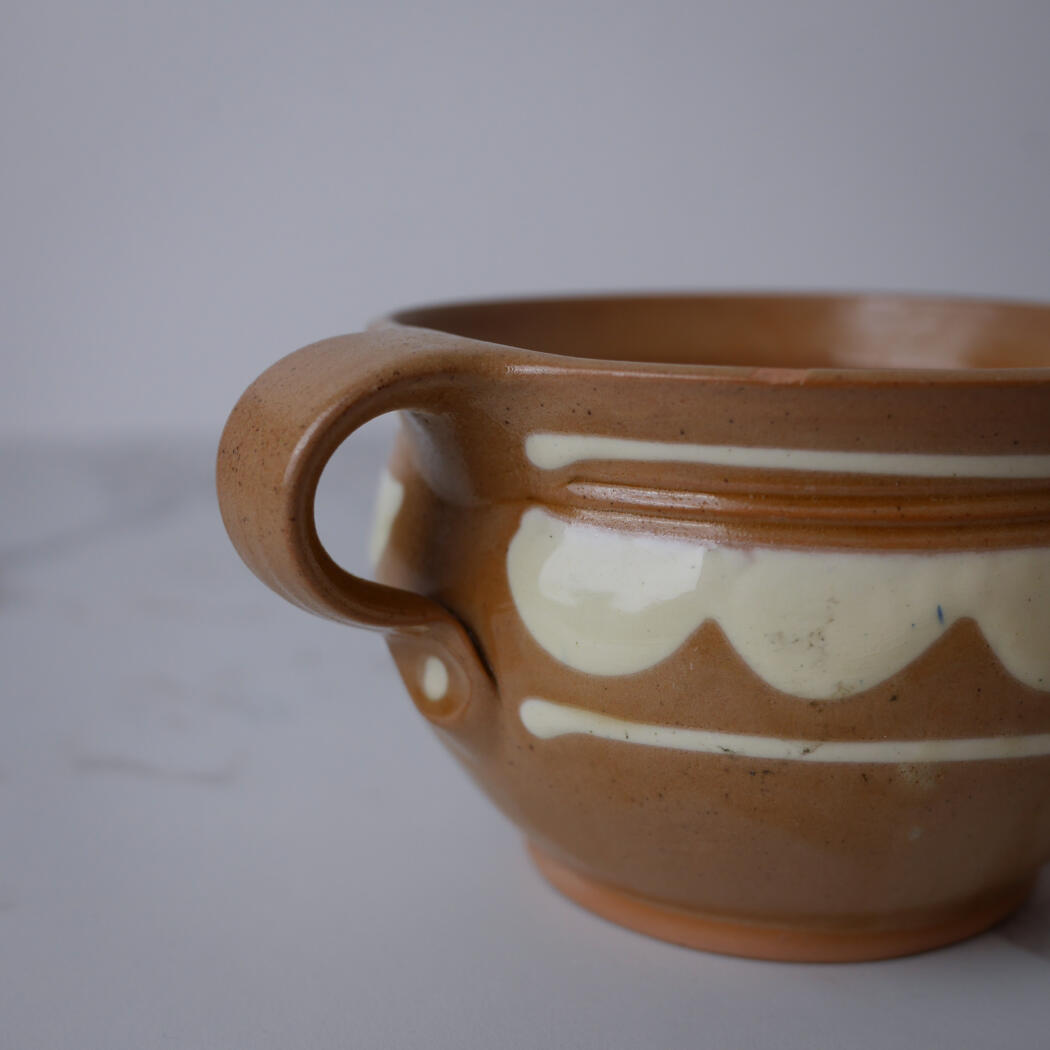 Close-up of a brown ceramic mug with a white wavy glaze pattern around its middle, viewed from the side.