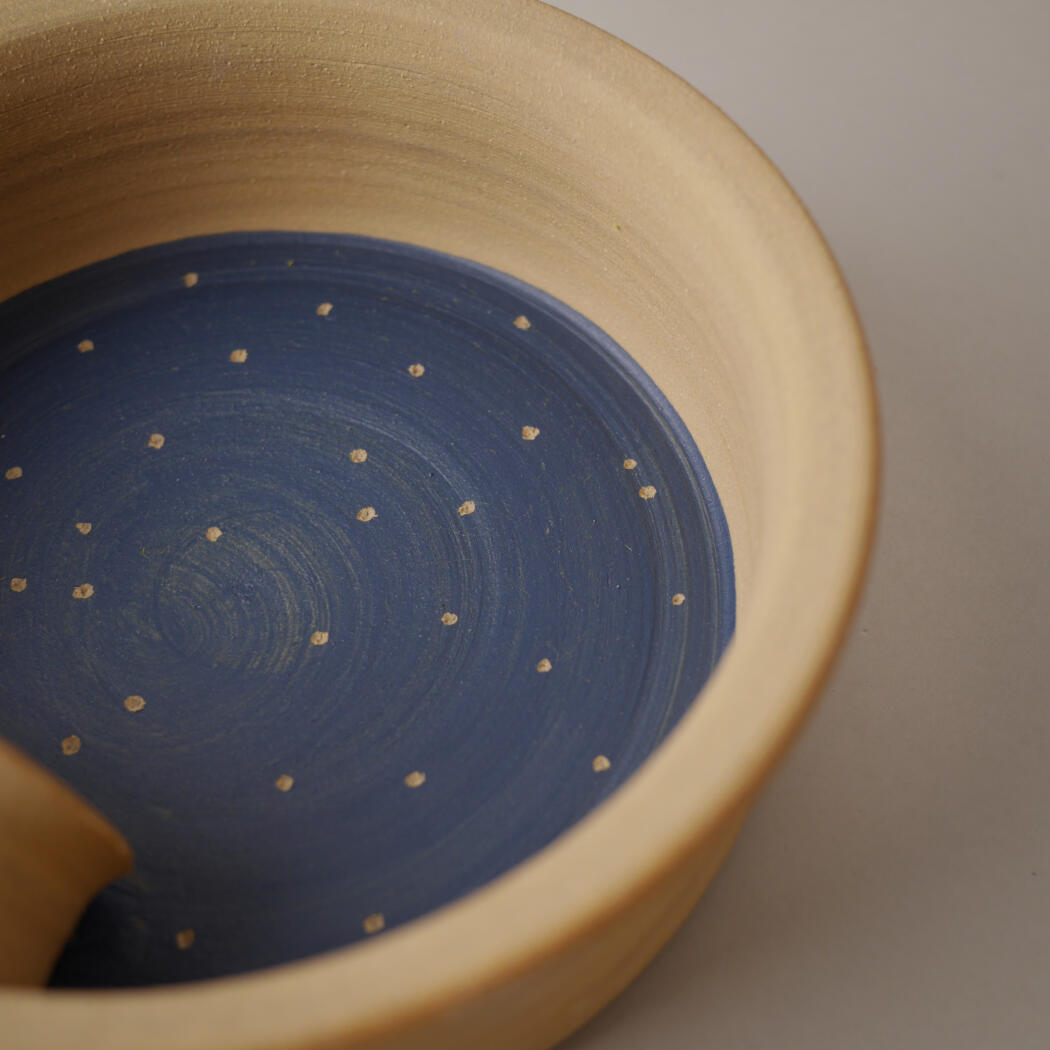 Close-up of a light tan ceramic bowl with a blue glazed interior dotted with small white specks.