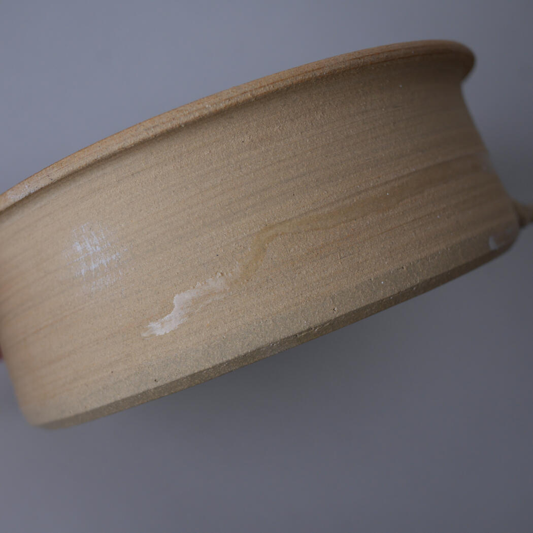 Close-up of a light brown ceramic bowl rim, showing the smooth curved edge and subtle wheel marks.