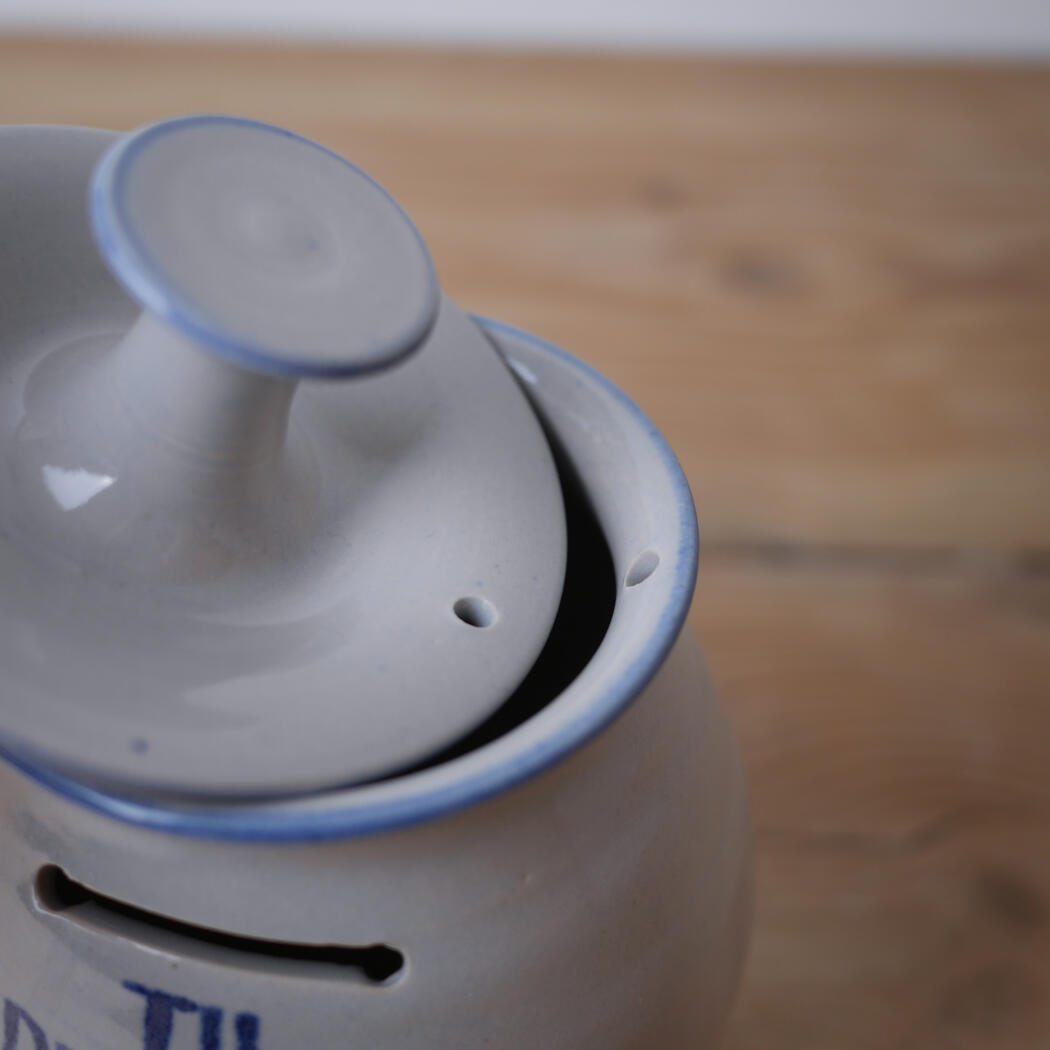 Close-up of a light gray ceramic teapot with a blue rim and lid slightly ajar on a wooden surface